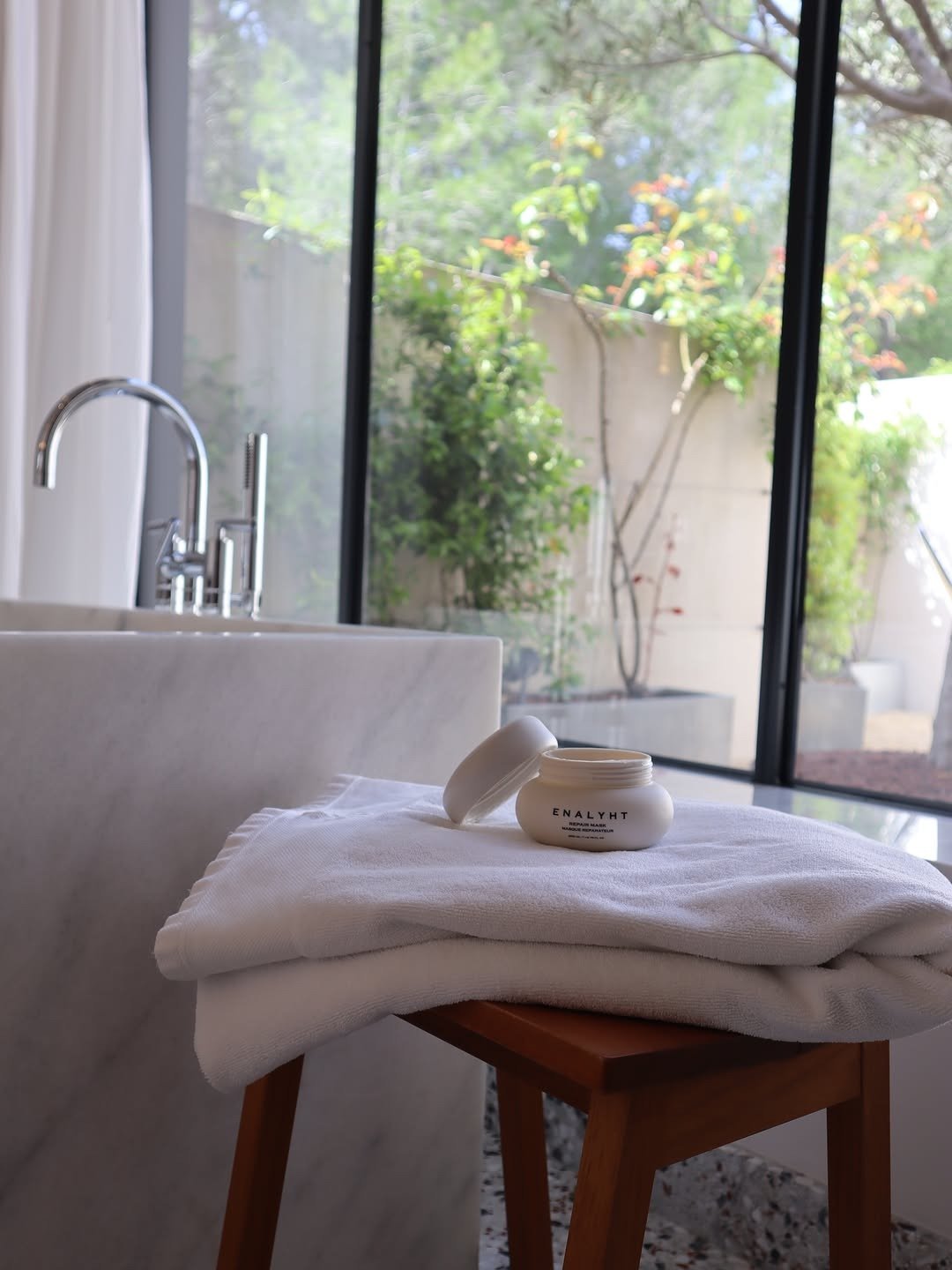 Open hair mask jar on towel beside bathtub