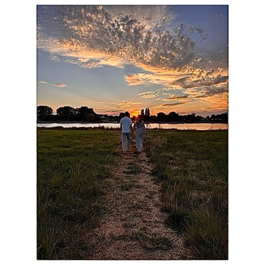 Couple walking hand in hand toward a river at sunset
