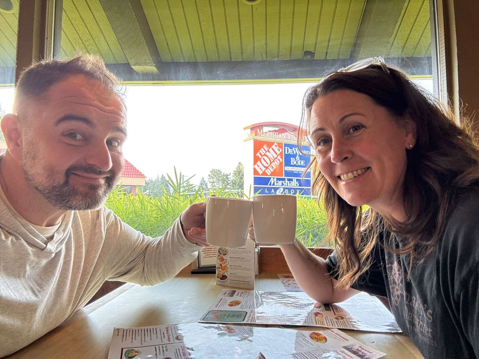 Couple toasting with coffee mugs at a restaurant table in morning light