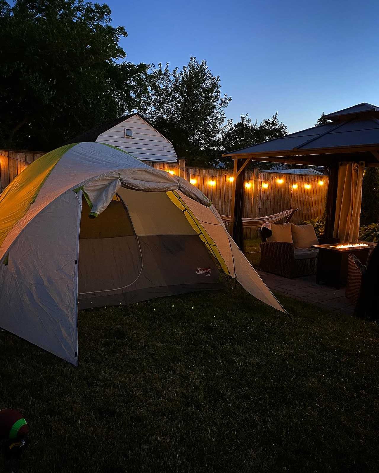 Tent glowing with string lights, fire table and hammock at dusk