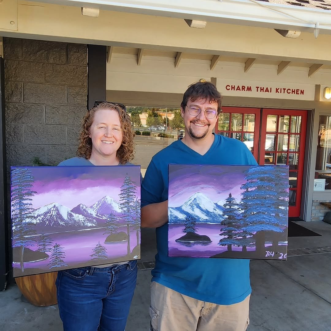 Couple holding up finished mountain paintings outside a studio