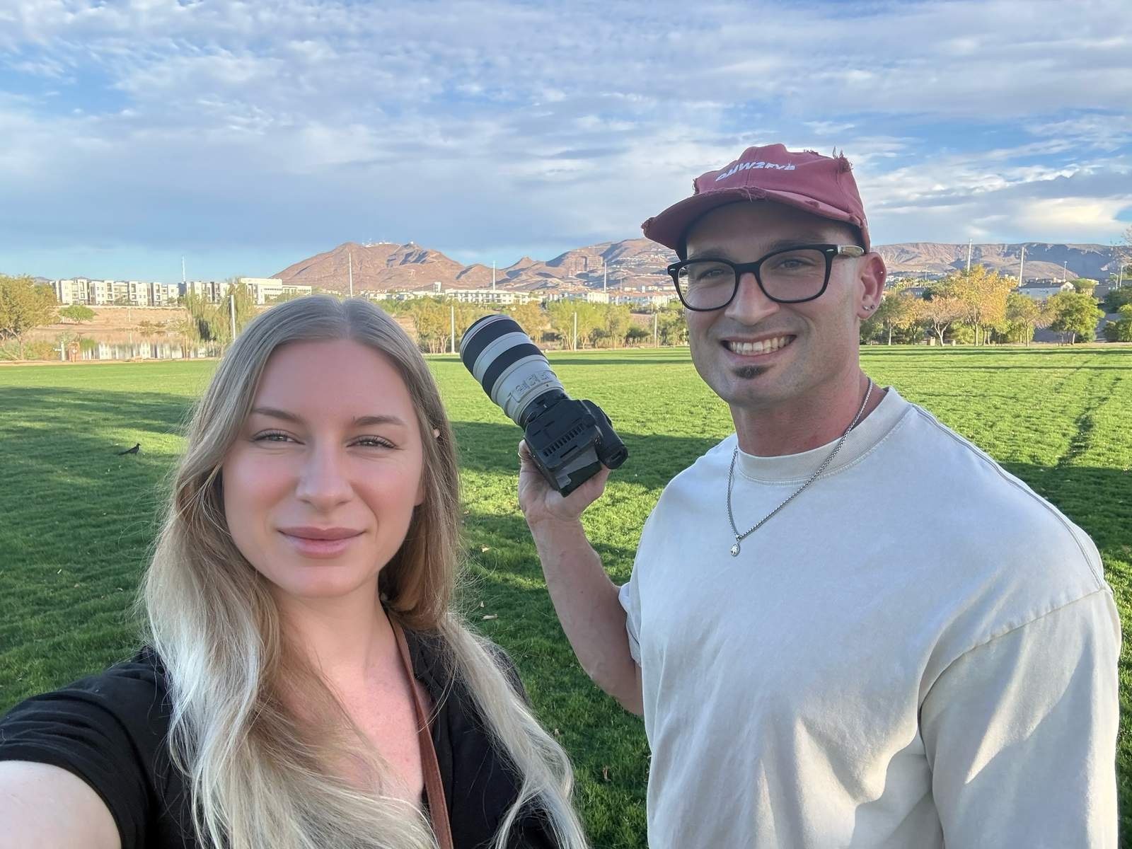 Couple taking a selfie in a park with a DSLR camera and mountains behind