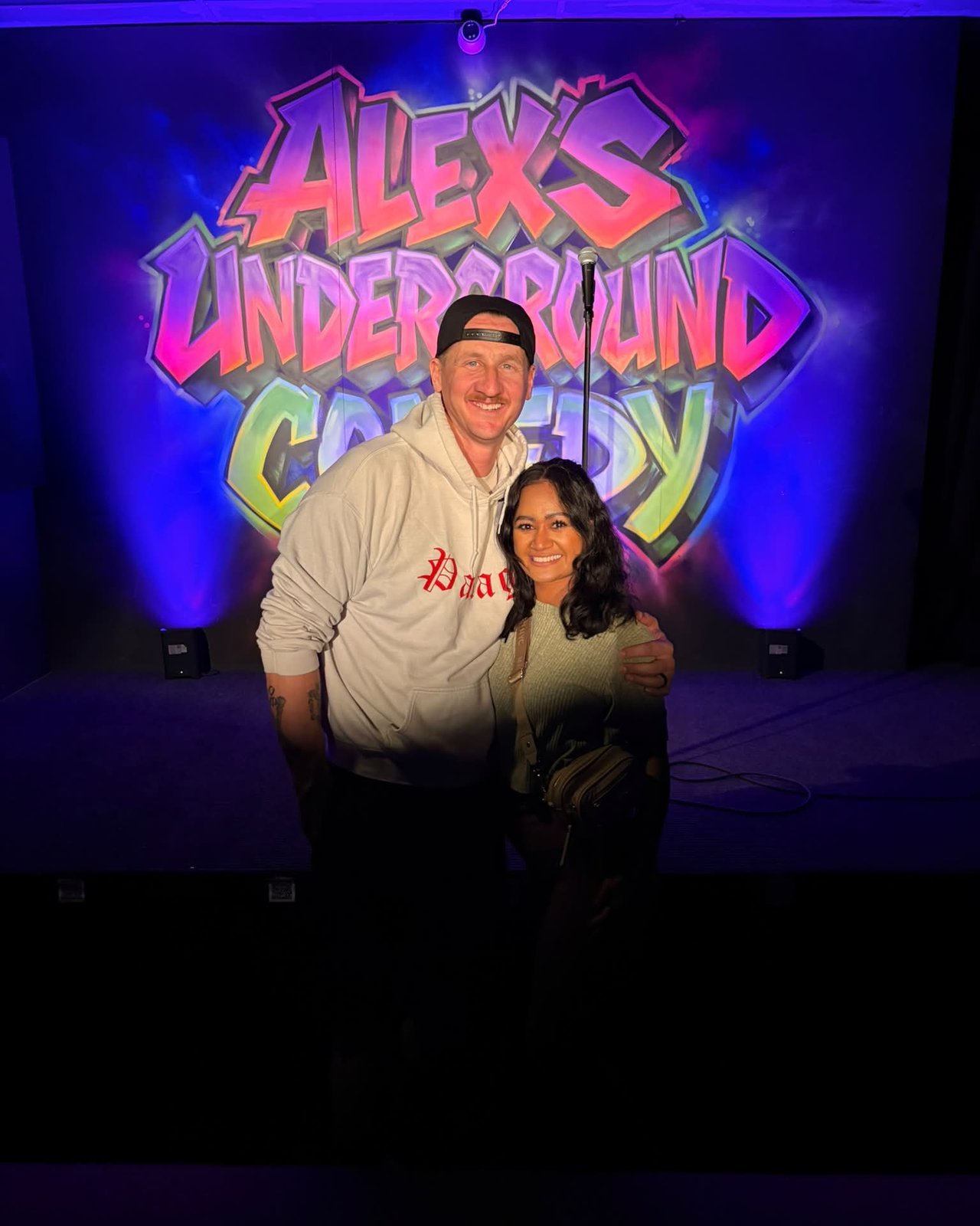 Married couple posing in front of a comedy club graffiti wall
