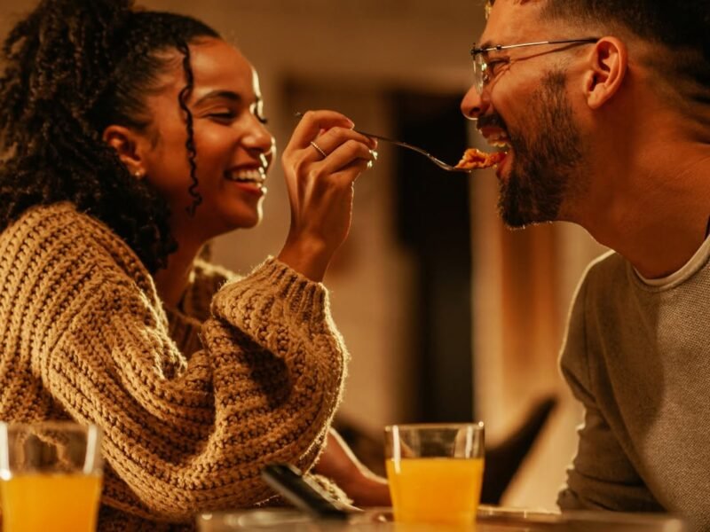 Couple laughing at dinner, woman playfully feeding her partner, no phones in sight