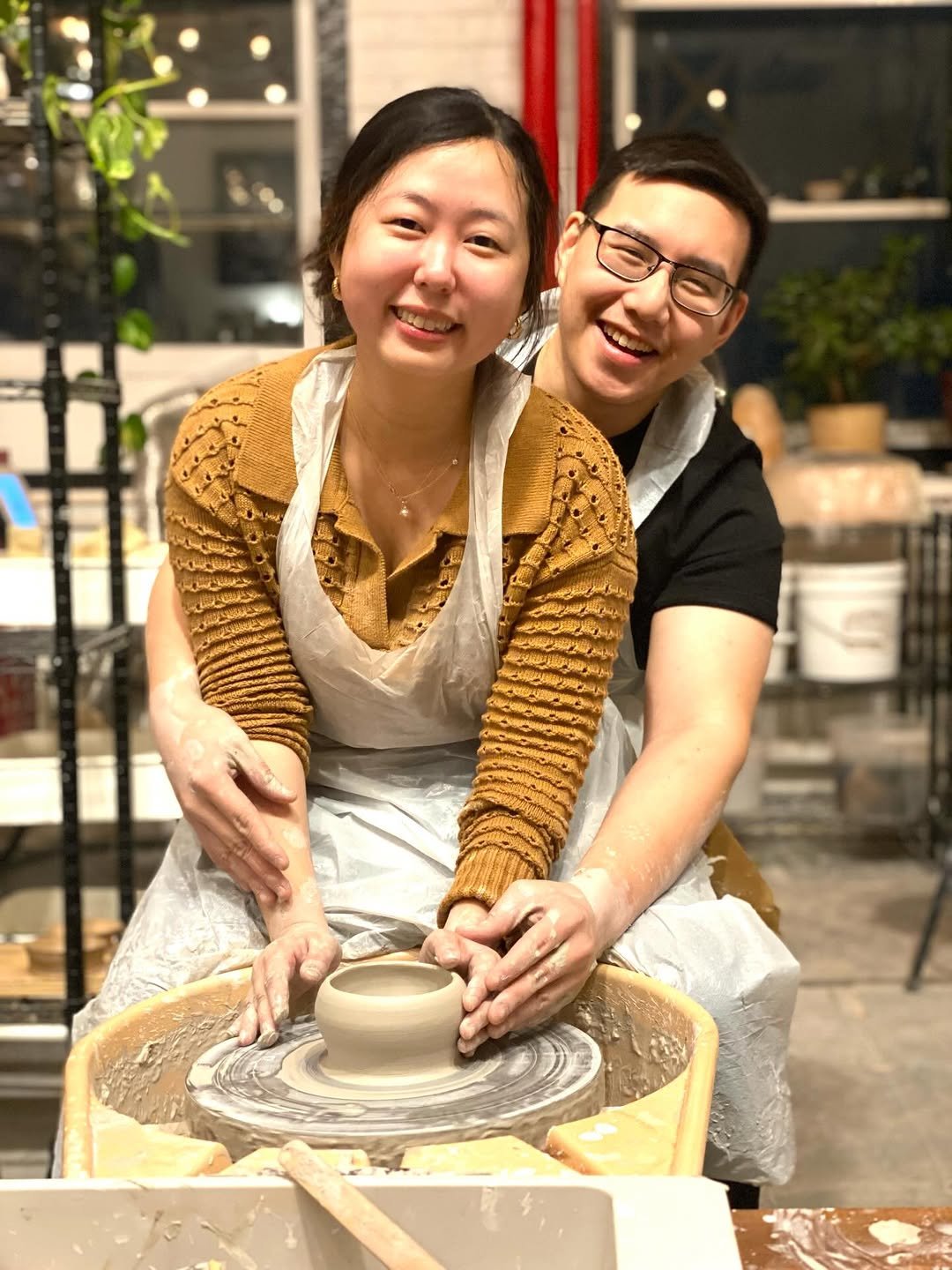 Couple at a pottery wheel, hands guiding each other shaping a clay bowl