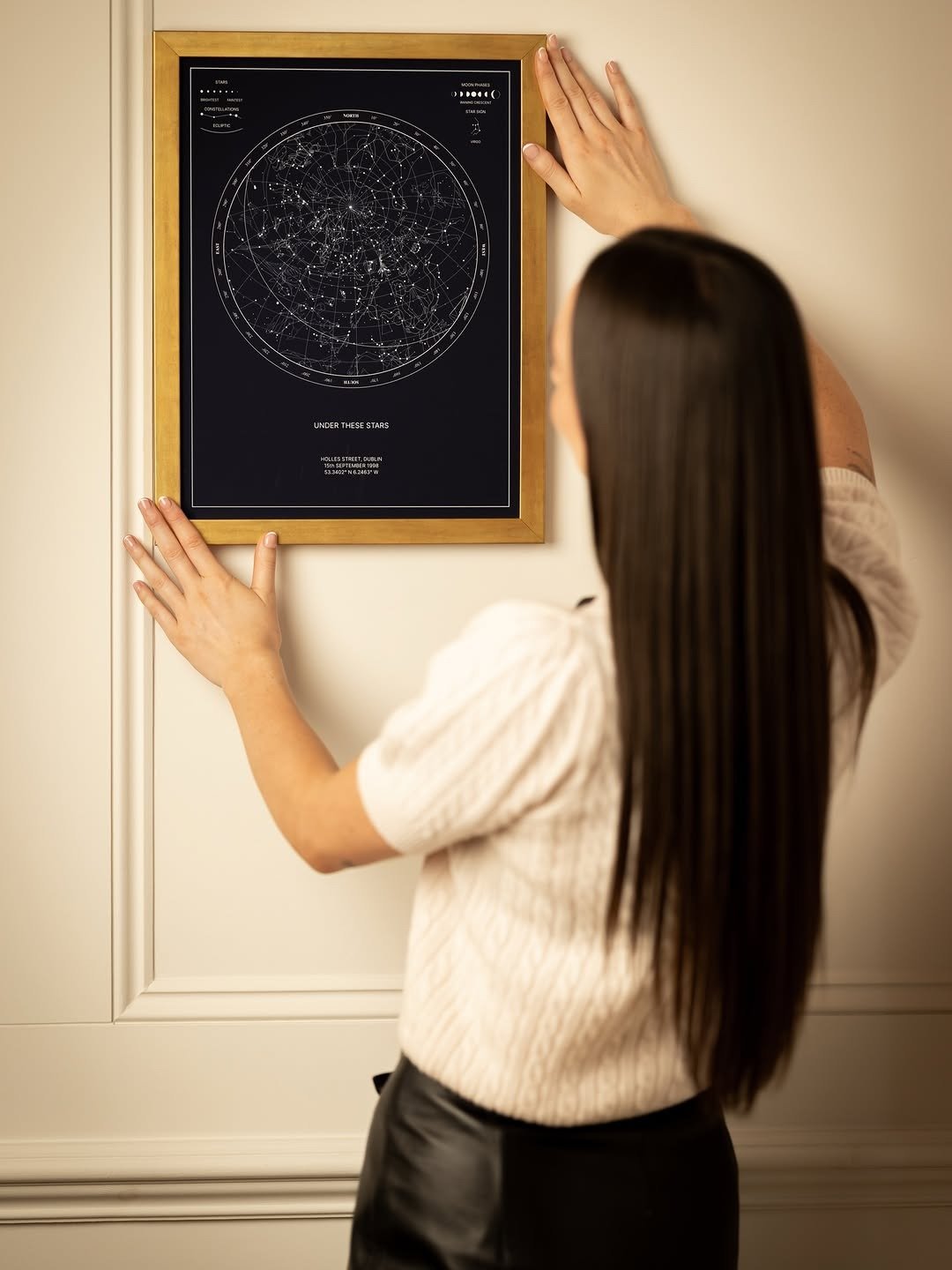 Woman hanging gold-framed star map print