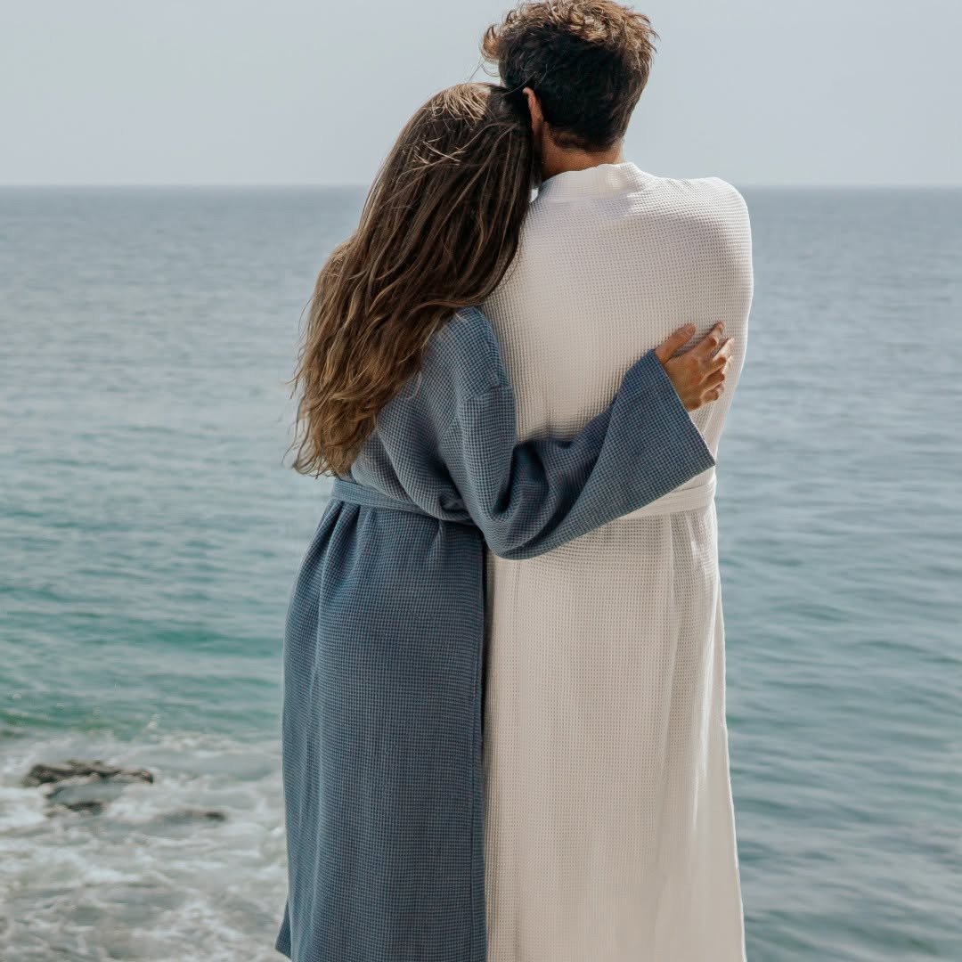 Couple embracing by the sea in matching waffle bathrobes