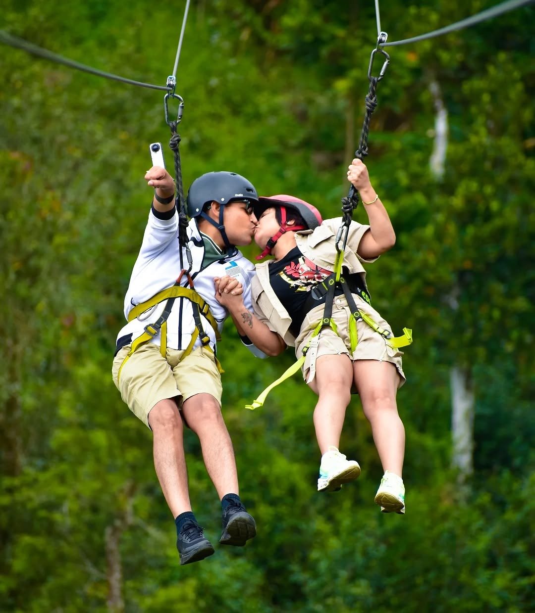 Couple zip lining side by side over forest