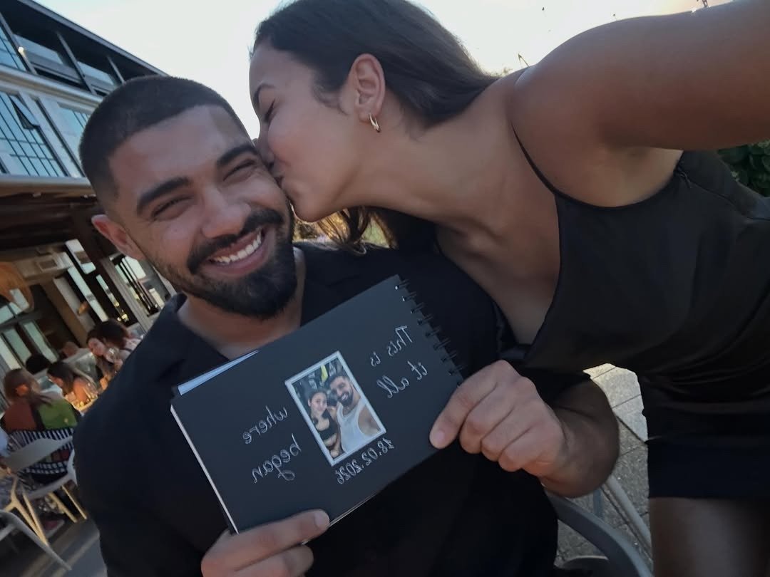 Man beaming holding his handmade birthday gift as girlfriend kisses his cheek