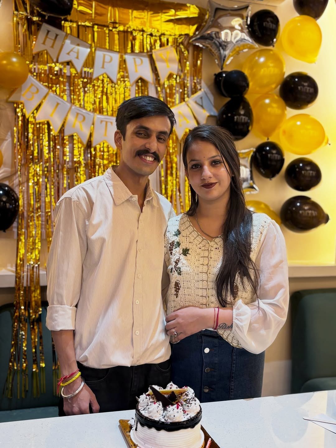 Couple at home with birthday banner, balloons and cake