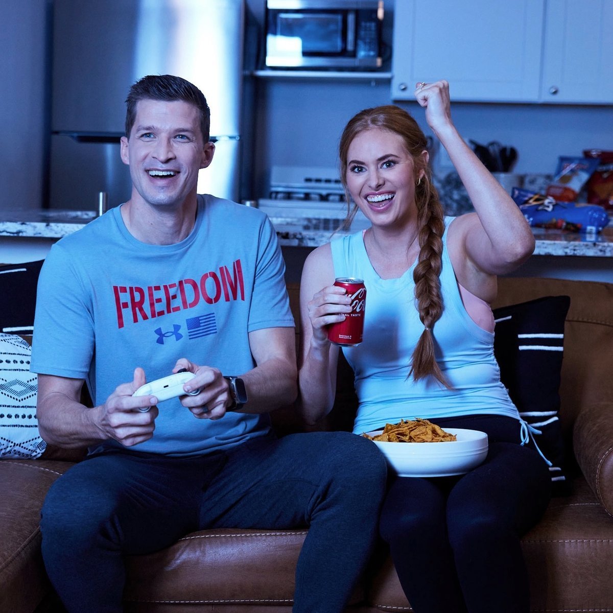 Couple on a couch playing a video game together, laughing and cheering