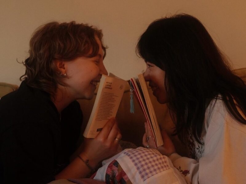 Couple snuggled on a couch under a patchwork quilt, laughing together face to face