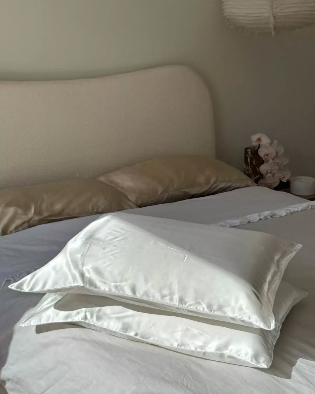 Stack of white silk pillowcases on a made bed