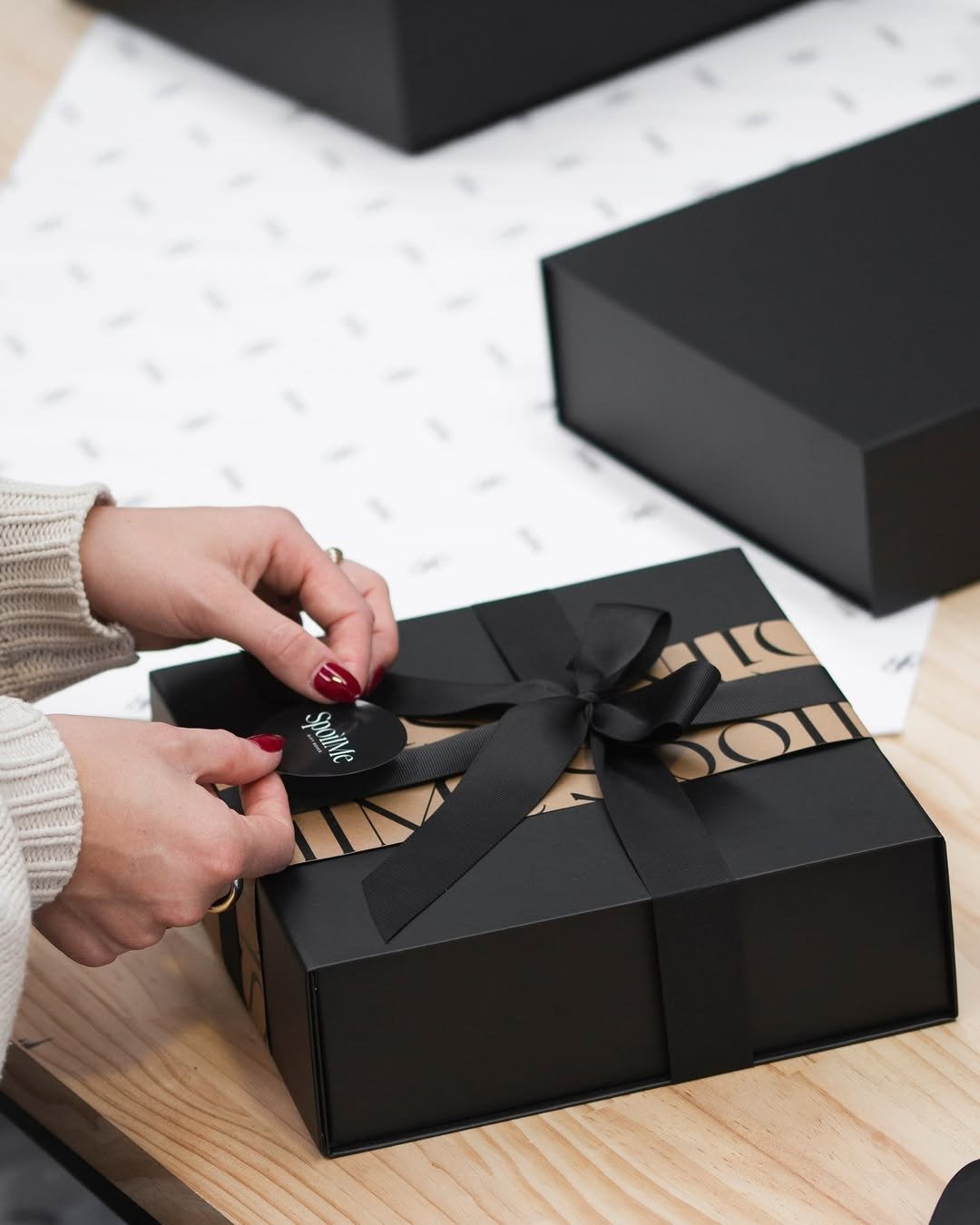 Hands finishing a ribbon bow on a gift box