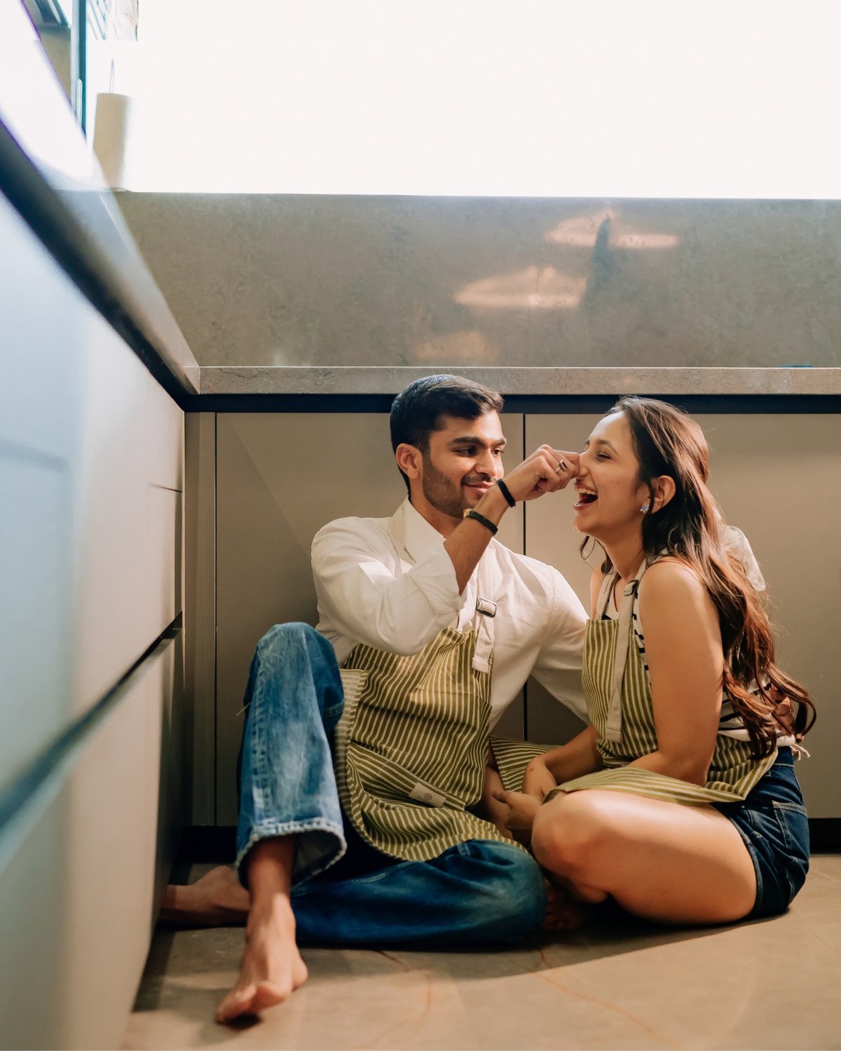 Couple in matching aprons laughing together on their kitchen floor