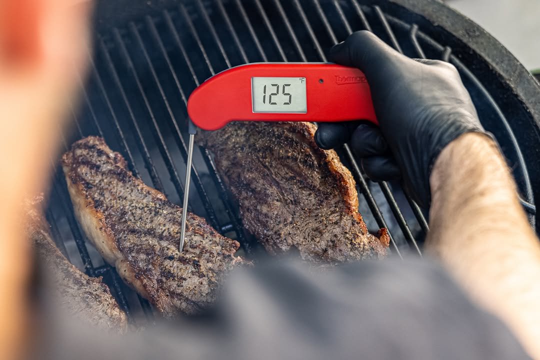 Instant-read thermometer in steaks on grill
