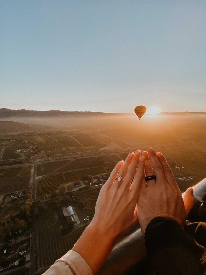 Couple hands over vineyards from balloon basket at sunrise