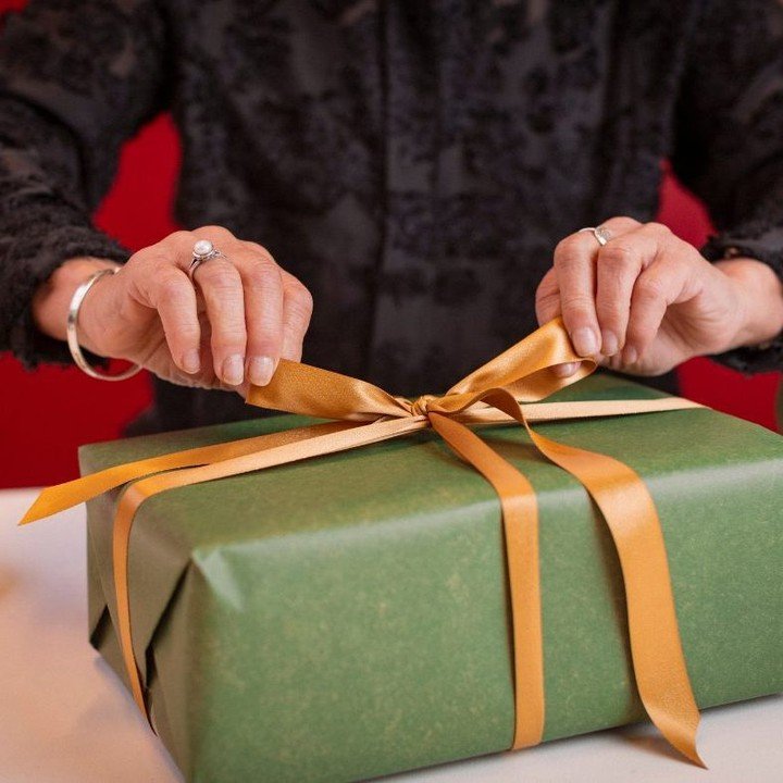Hands tying gold ribbon on wrapped gift box