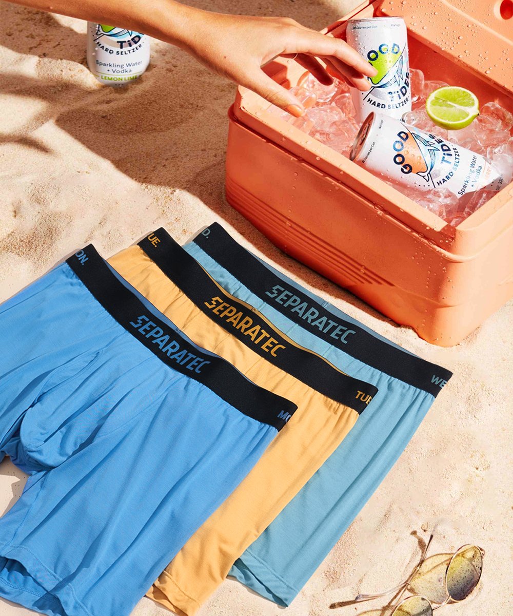Three pairs of bamboo boxer briefs on sand beside cooler