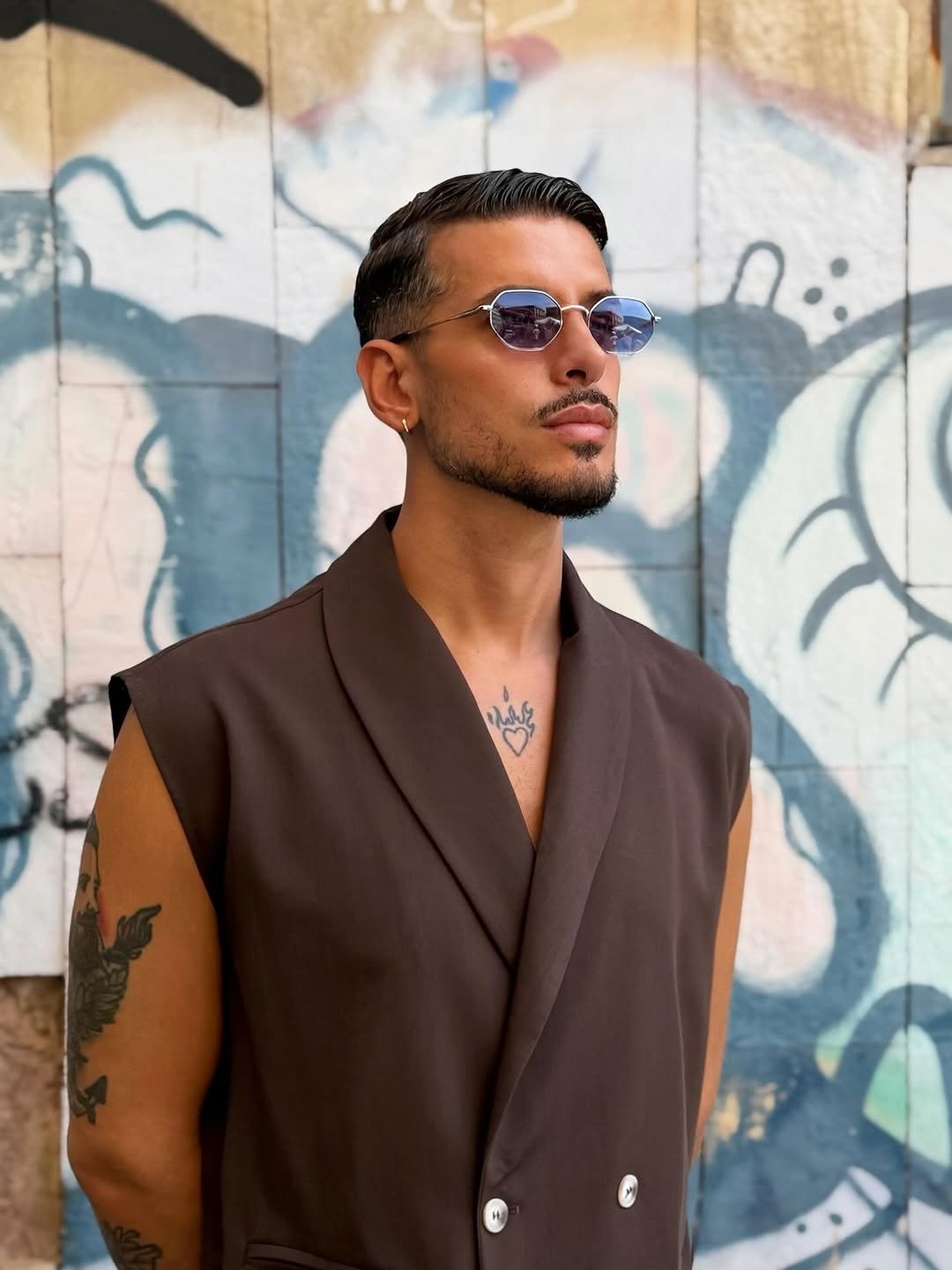 Man wearing round dark sunglasses against a graffiti wall
