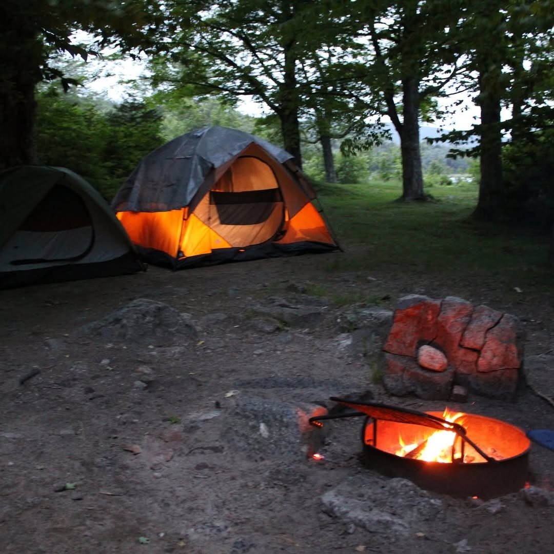Illuminated tent at wooded campsite at dusk with campfire