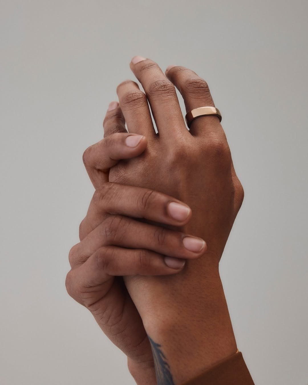 Gold Oura smart ring on finger, clasped hands