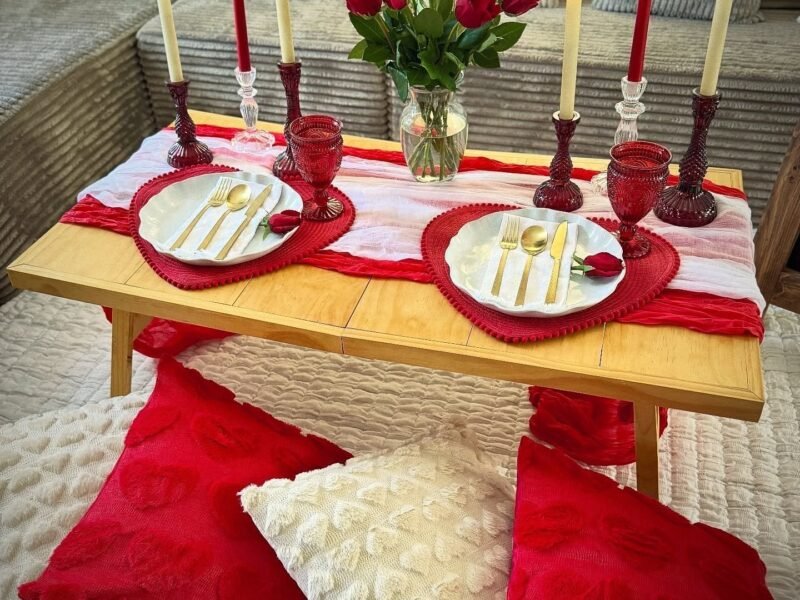 Low wooden table with candles, red roses and floor pillows set for two