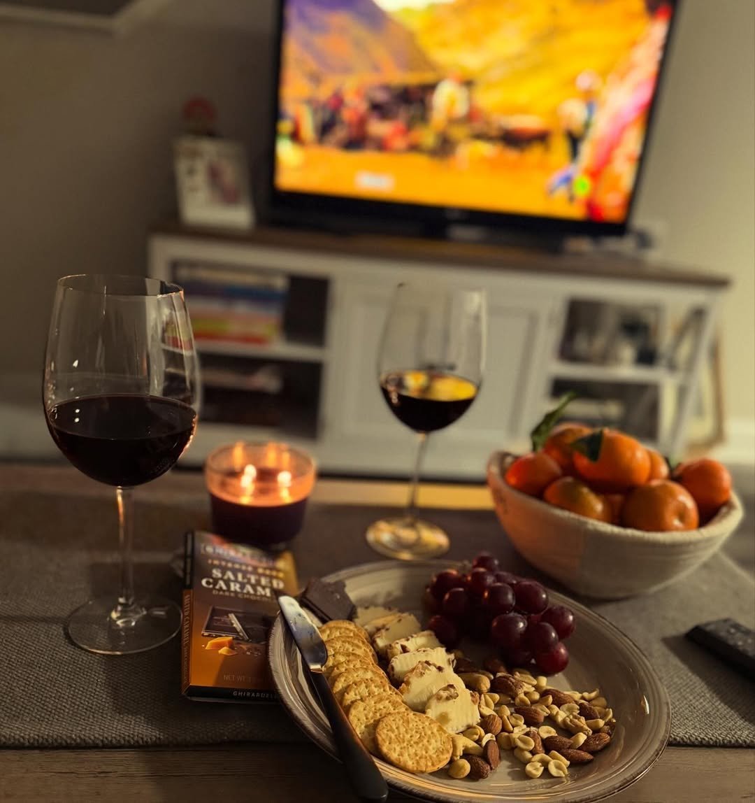 Two wine glasses with cheese plate, candle and chocolates by the TV