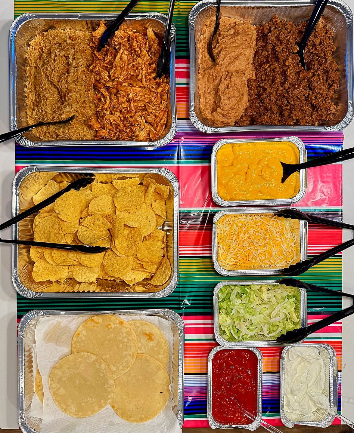 Taco bar with trays of fillings on a colorful striped tablecloth