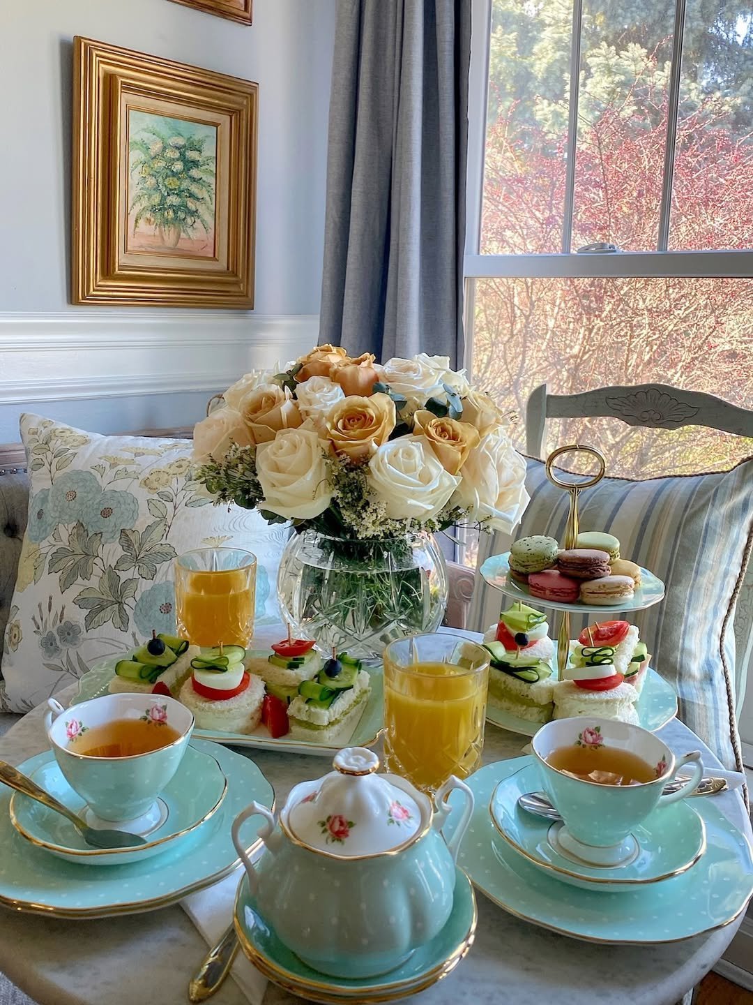Afternoon tea with floral teapot, tiered treats and roses by a window