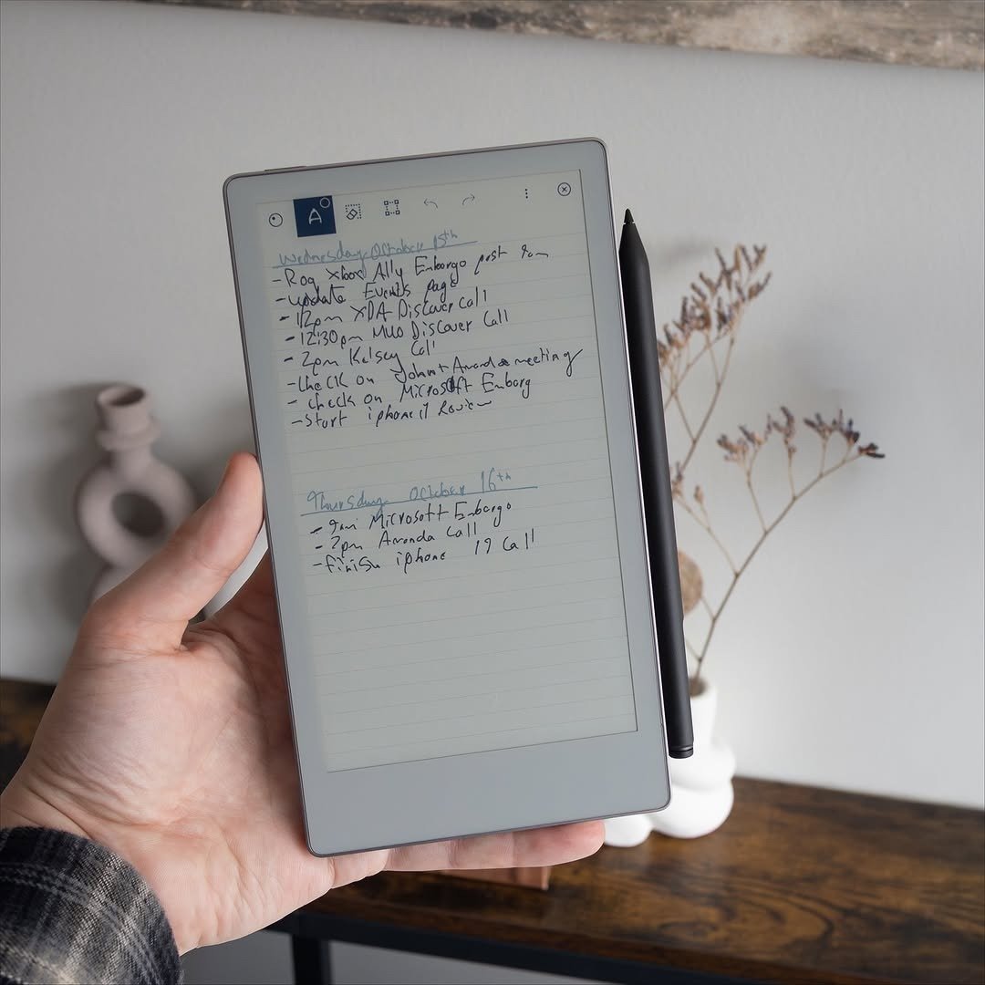 Hand holding e-ink tablet with stylus and notes