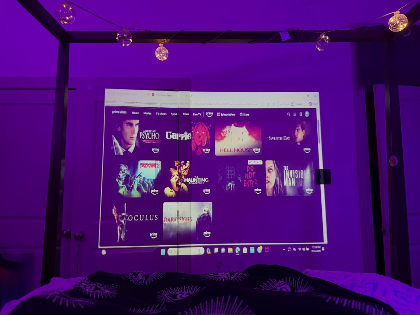 Movie projected on a wall in a cozy bedroom with string lights
