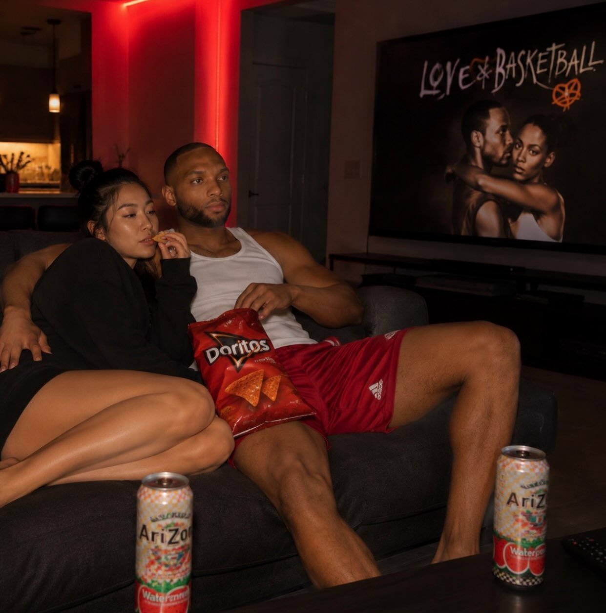 Couple cuddled close on a couch watching TV with snacks