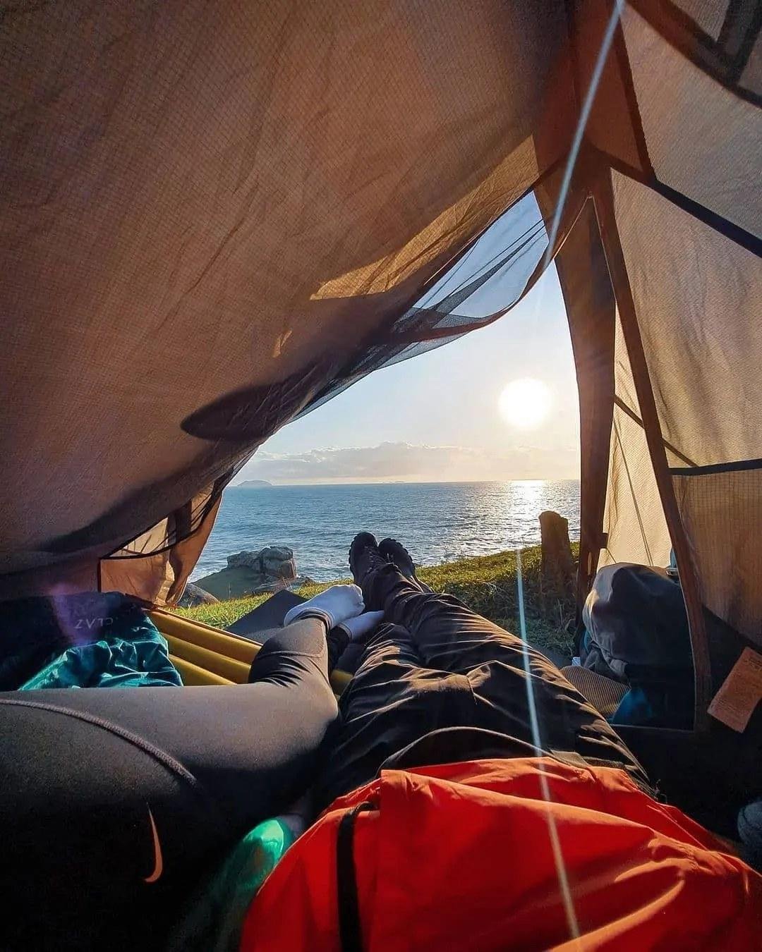 Two people lying in a tent looking out at a sea view
