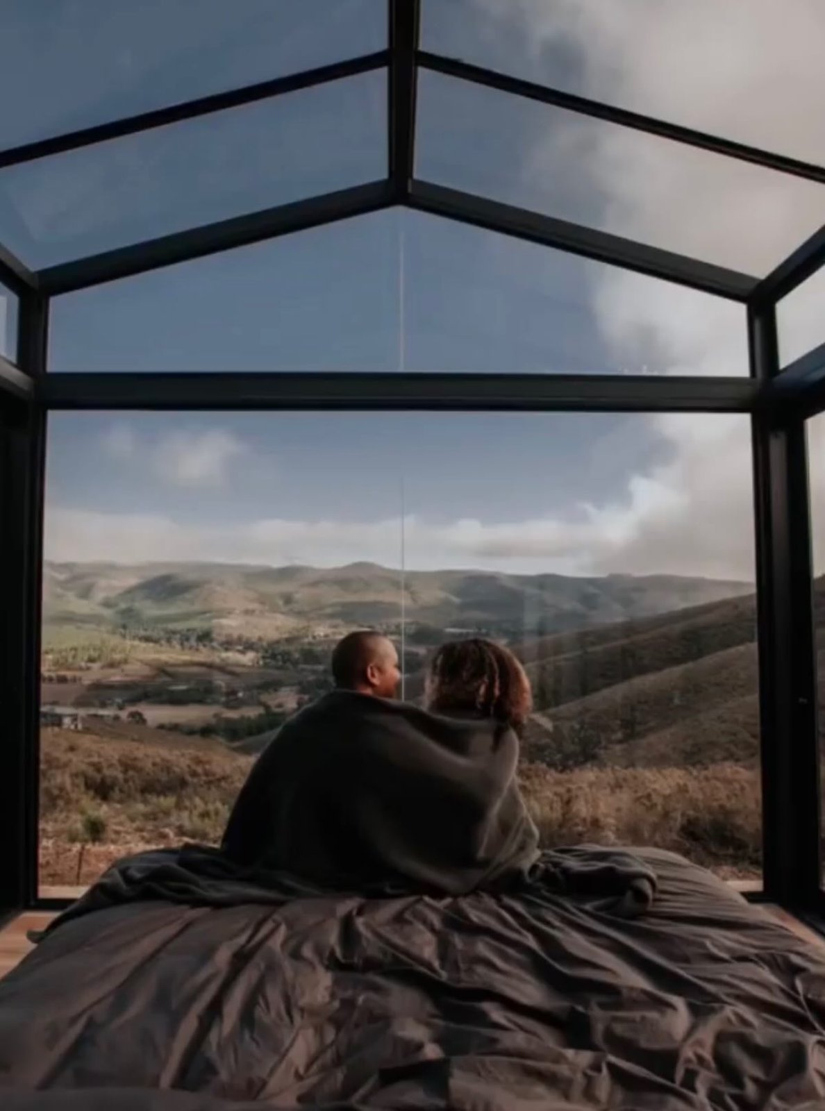 Couple wrapped in a blanket inside a glass-walled cabin