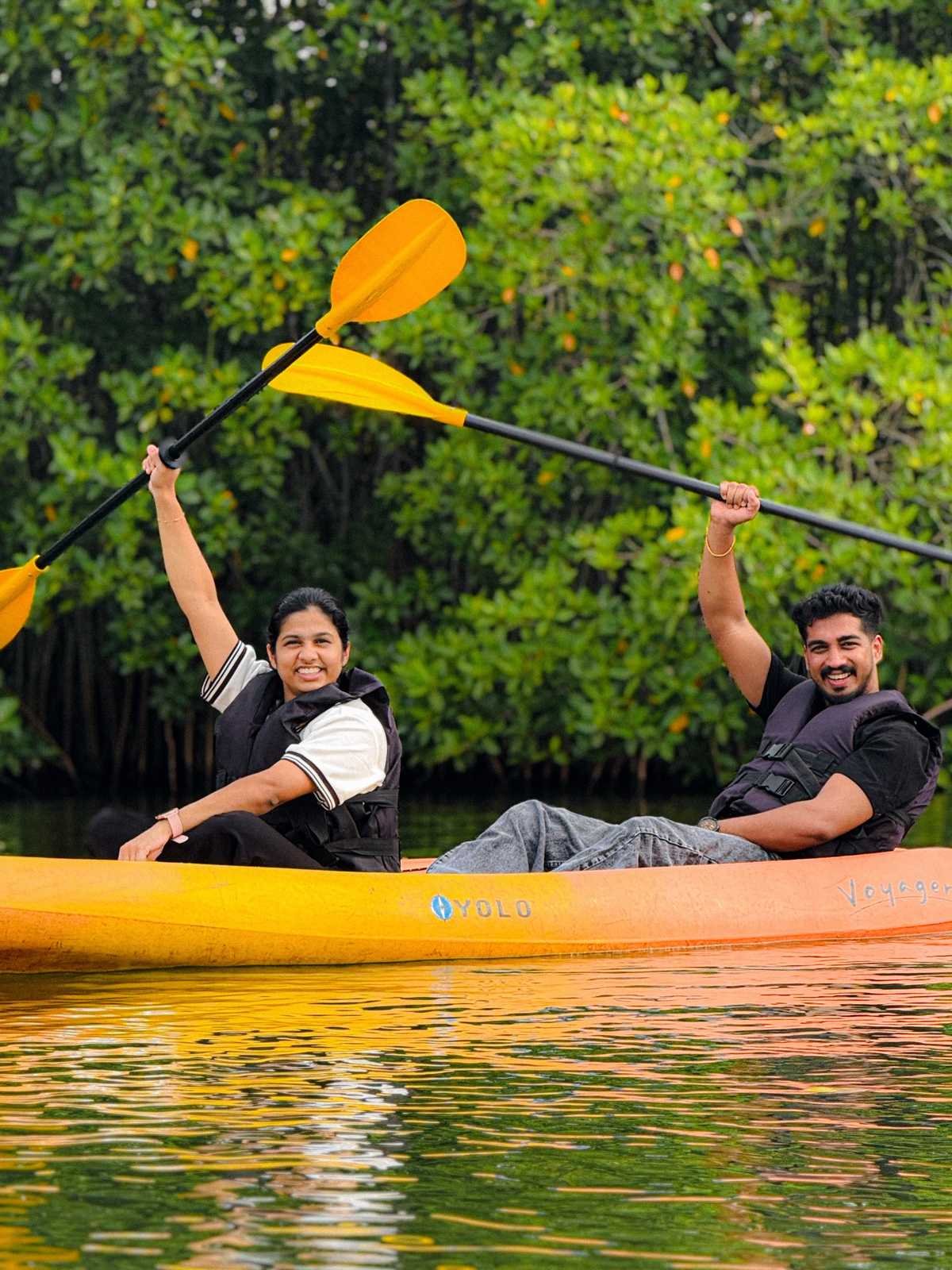 Couple in a yellow kayak on calm water holding paddles up