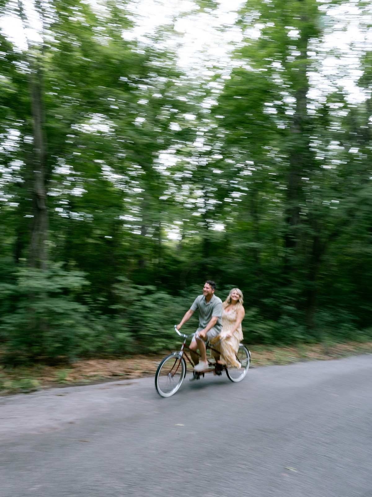 Couple riding a tandem bicycle on a tree-lined road
