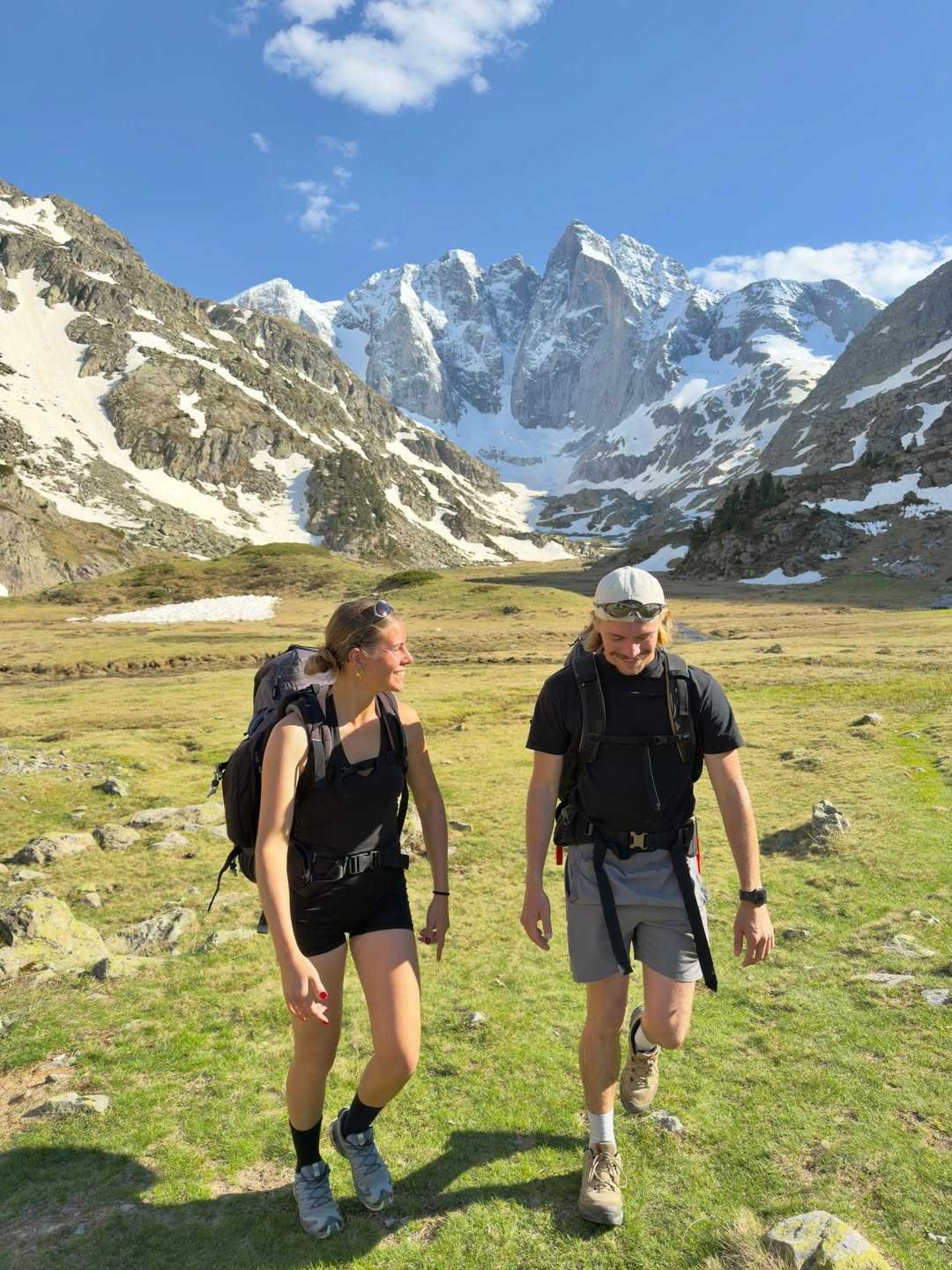 Couple with backpacks walking through a sunny alpine meadow
