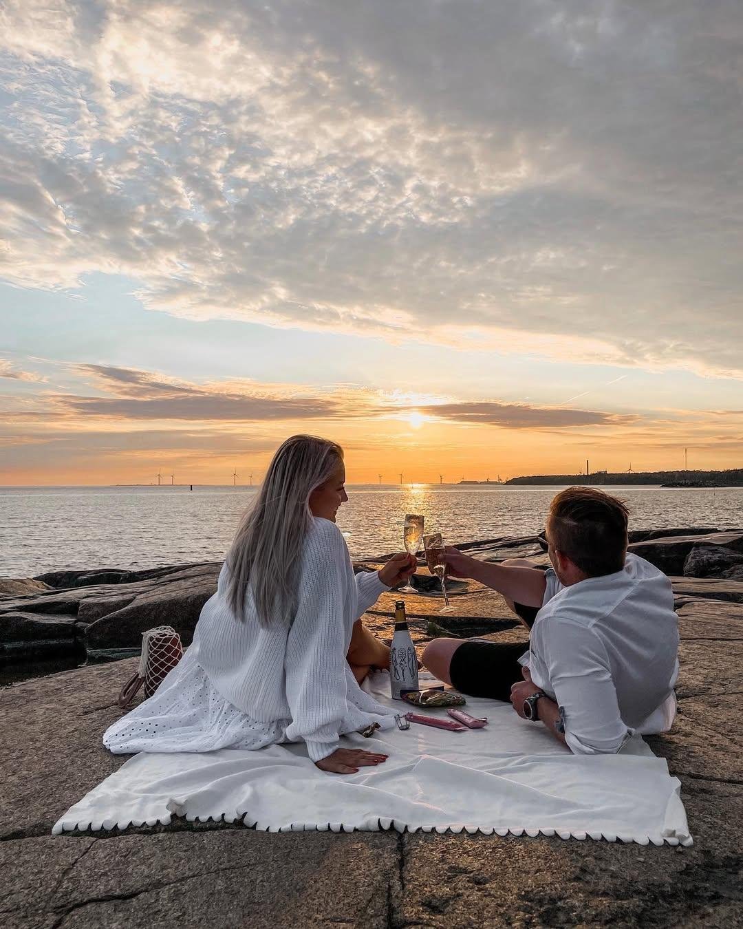 Couple toasting champagne glasses on a picnic blanket at sunset
