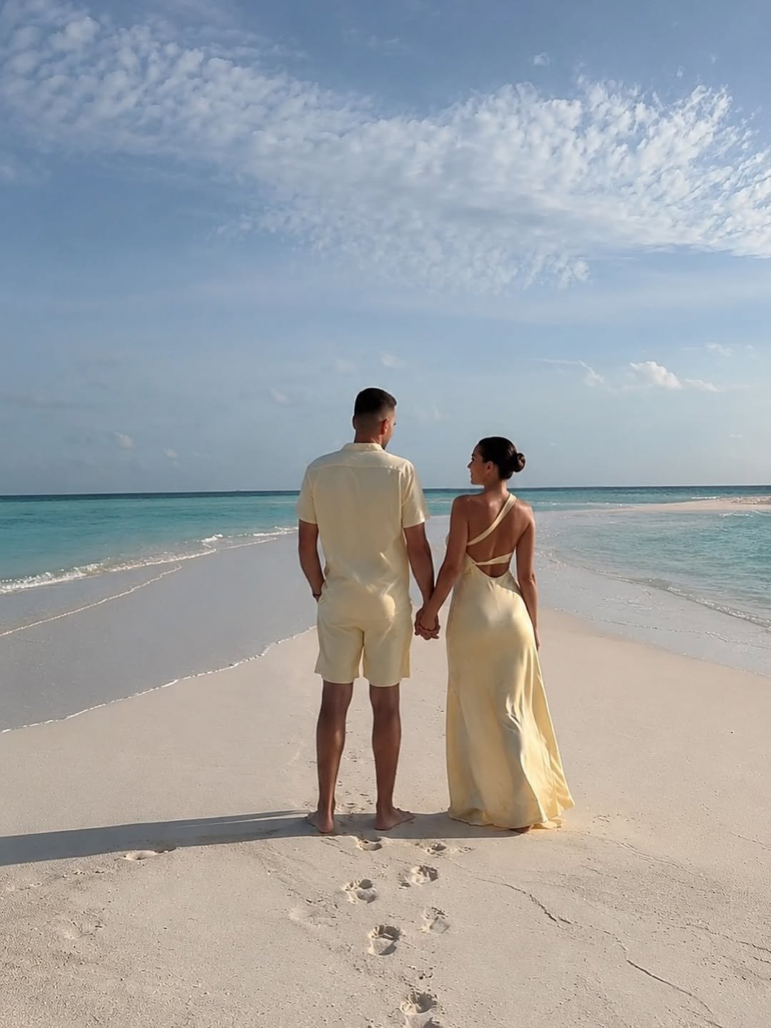 Couple holding hands on a white-sand beach facing the ocean