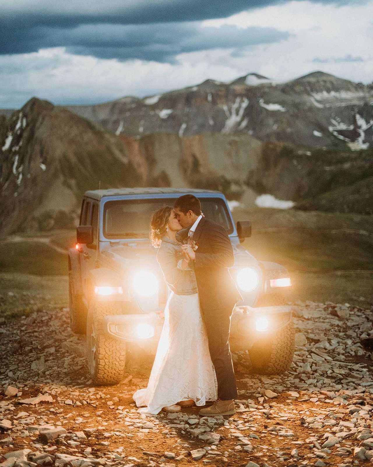 Couple embracing in front of a Jeep at dusk with mountains behind