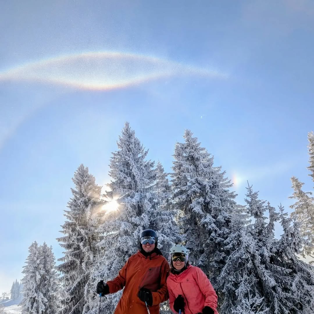 Couple in ski gear posing in front of snow-covered pines