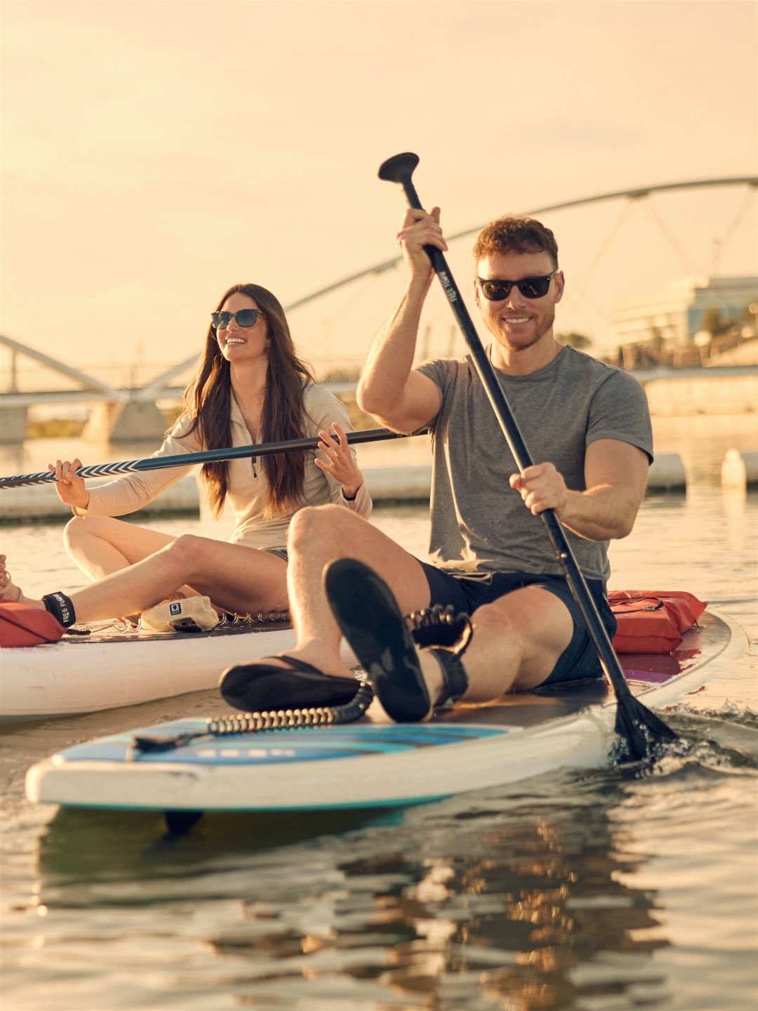 Smiling couple paddleboarding across a lake at golden hour