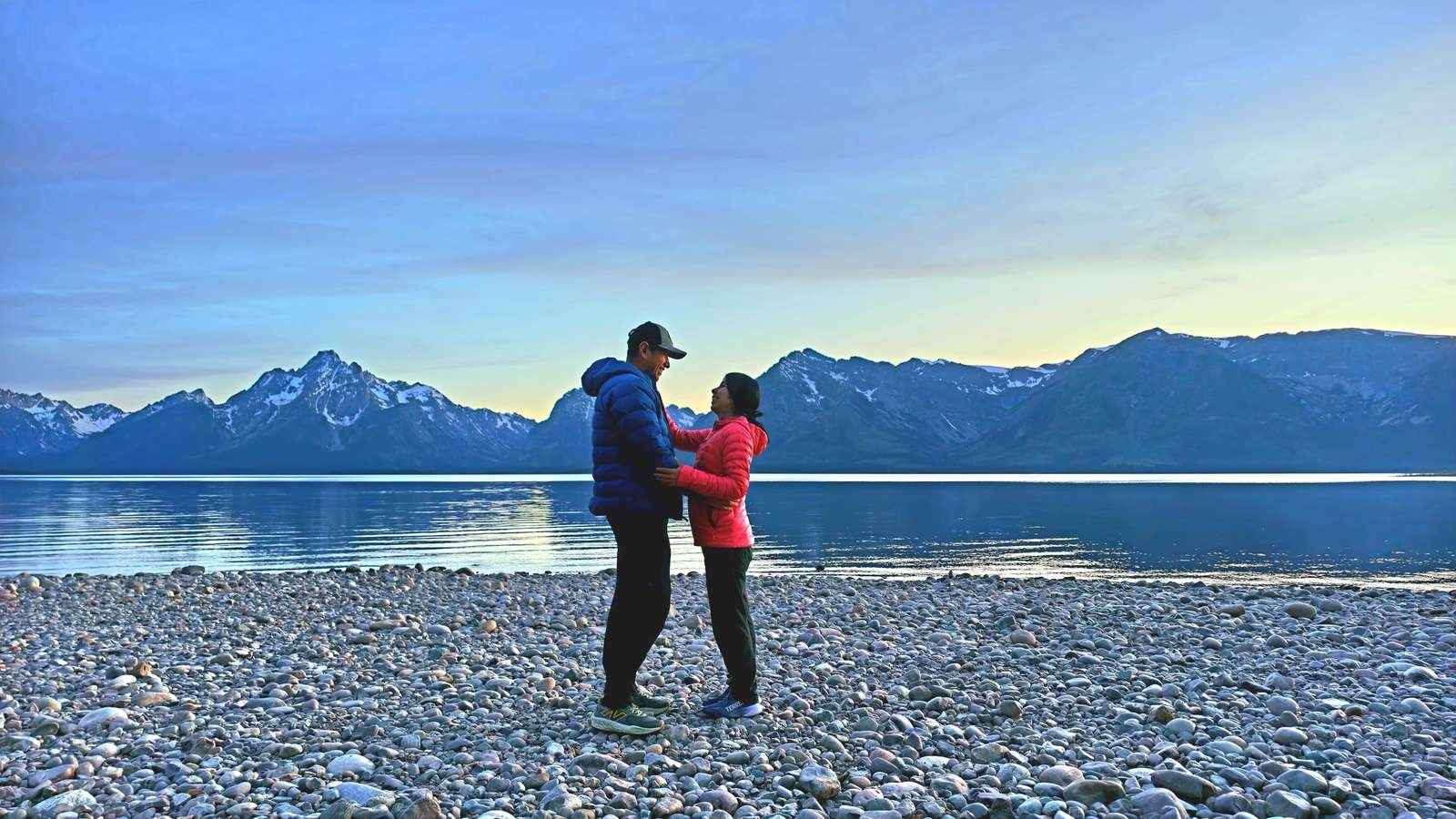 Couple embracing on a rocky lakeshore with mountains at sunset