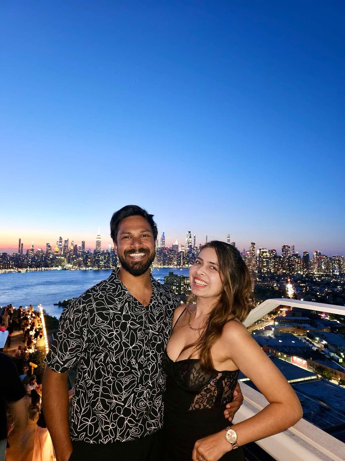 Smiling couple at a rooftop bar with a city skyline at dusk