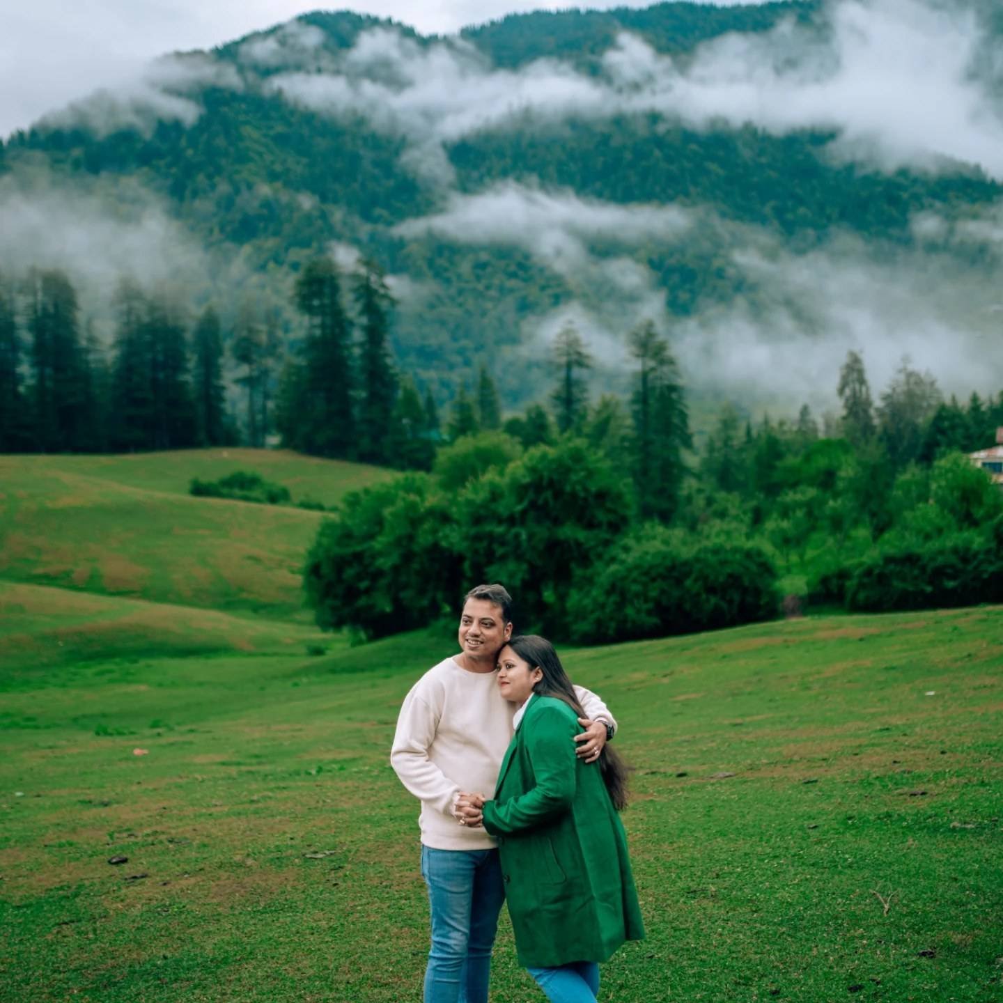 Couple embracing in a green meadow with misty mountains