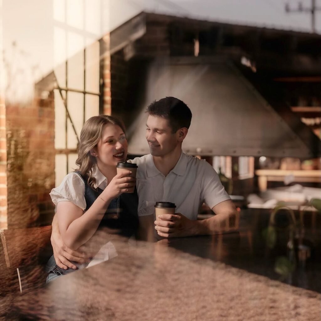 Couple at a cafe counter holding takeaway coffees, laughing and talking together
