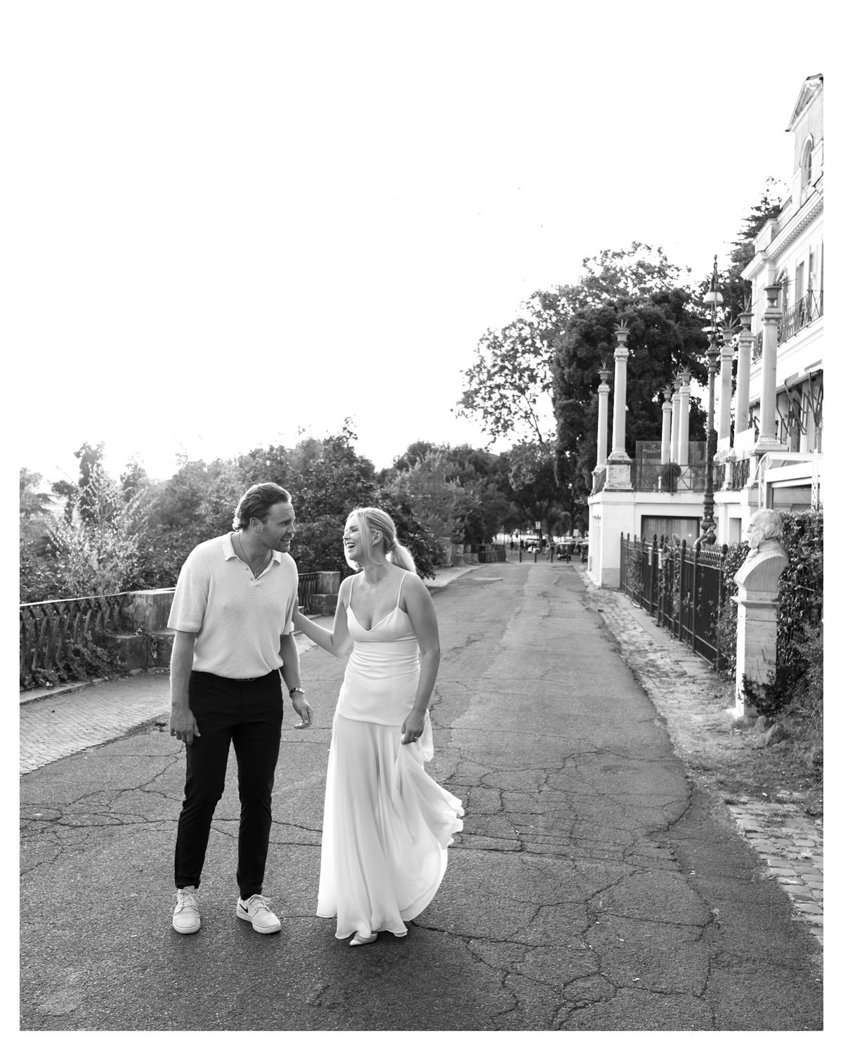 Black and white photo of a couple walking down a quiet street, turned toward each ot