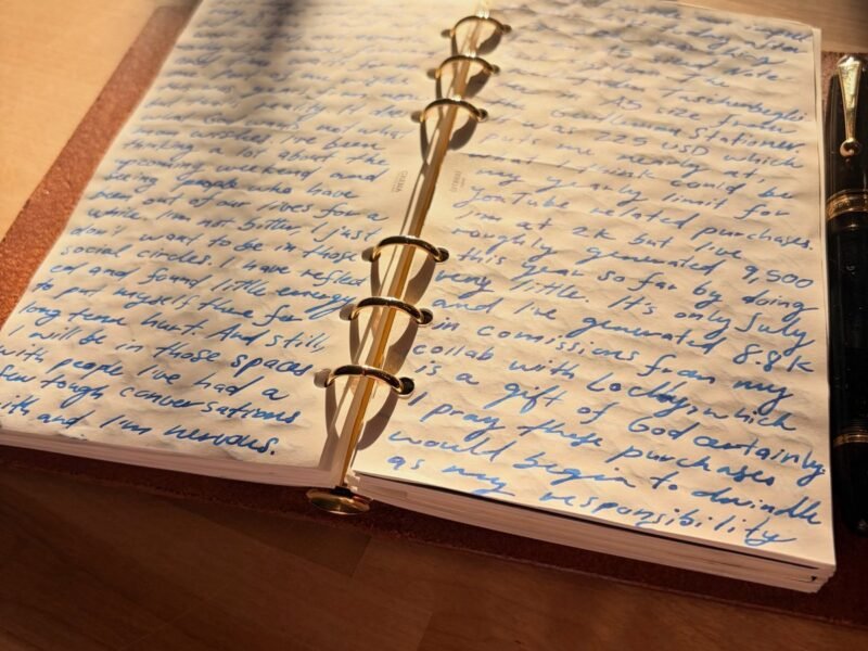 Open journal filled with handwriting on a sunlit wooden table, a fountain pen resting beside it