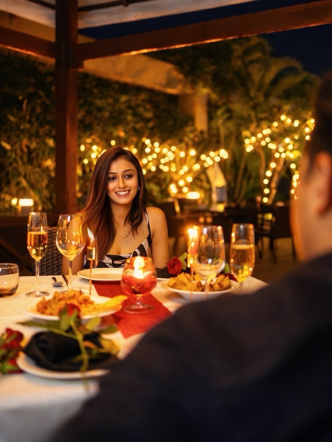Woman enjoying a candlelit dinner for two with wine and fairy lights